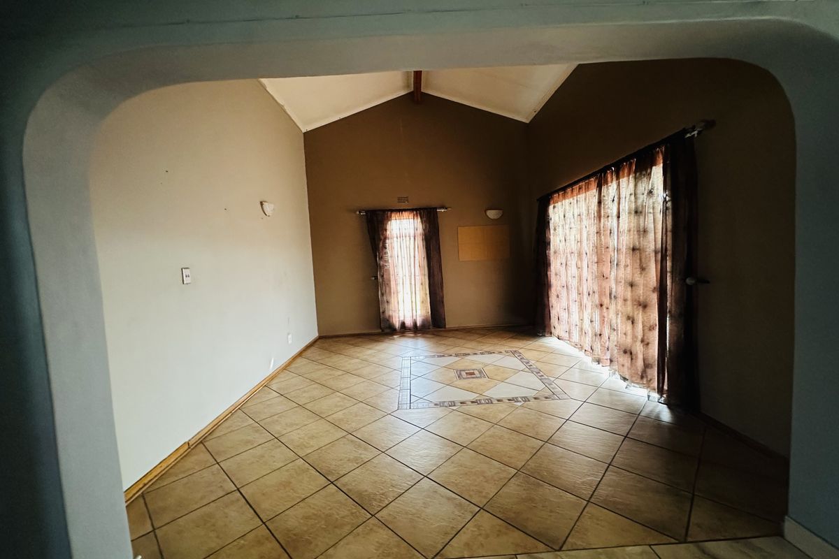 Spacious living area featuring a vaulted ceiling, tiled flooring with a decorative inlay, and large sliding glass doors providing natural light.