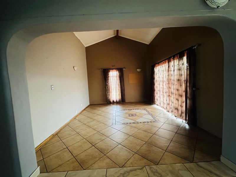 Spacious living area featuring a vaulted ceiling, tiled flooring with a decorative inlay, and large sliding glass doors providing natural light.