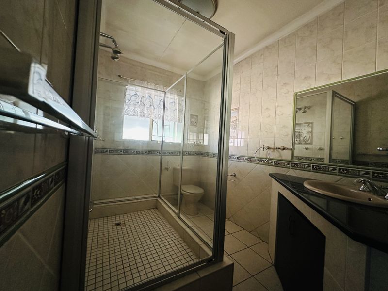 A functional bathroom featuring a glass-enclosed shower, a vanity with a dark countertop, and neutral wall tiling throughout.