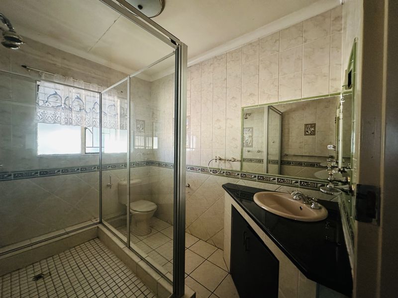 A functional bathroom featuring a glass-enclosed shower, a built-in vanity with a granite countertop, and neutral wall and floor tiling.