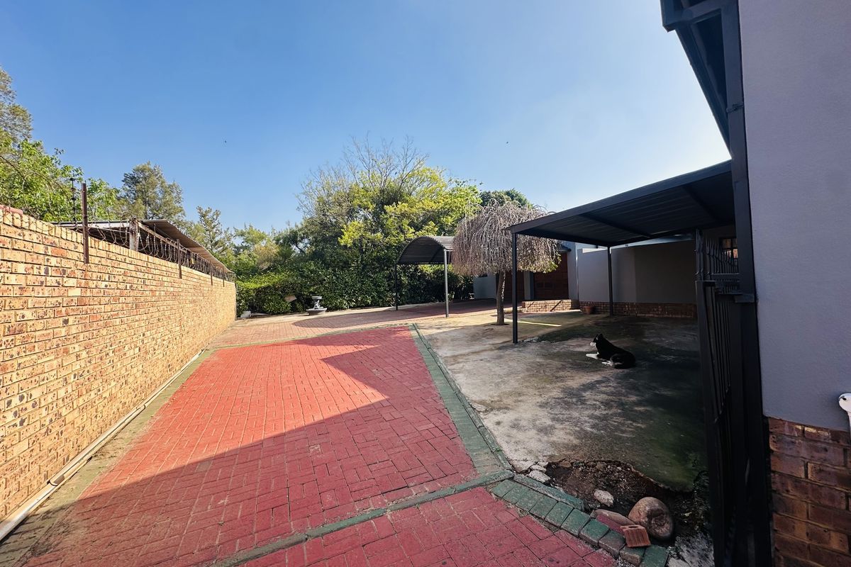 Rear exterior area featuring a paved driveway, brick boundary wall, and a covered carport structure.