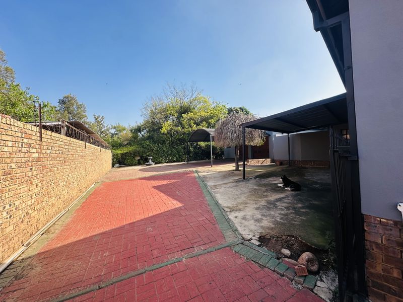 Rear exterior area featuring a paved driveway, brick boundary wall, and a covered carport structure.