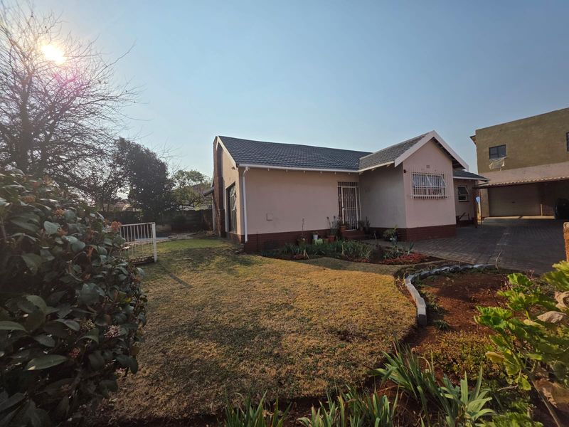 Front view of a single-story house featuring a tiled roof, paved driveway, and established garden area.