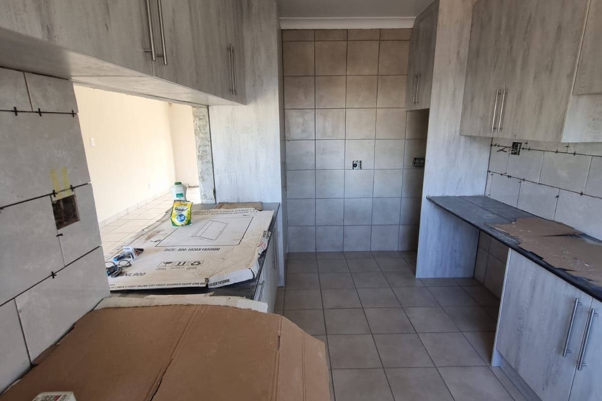 An unfinished kitchen space featuring light wood-look cabinetry, tiled flooring, and tiled splashbacks, currently undergoing renovation with exposed electrical points.