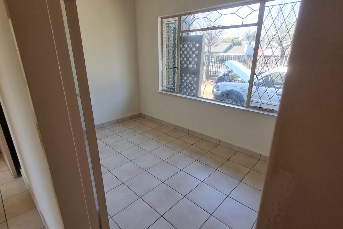 A vacant bedroom featuring neutral tiled flooring, a large window with security bars, and a simple ceiling light fixture.