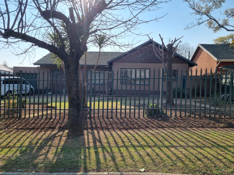 Front view of a single-story house featuring a tiled roof, brick facade, and secure spiked metal perimeter fencing with a front lawn.