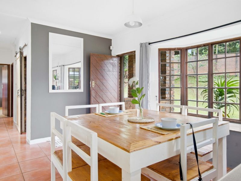 A bright dining area featuring terracotta floor tiles, a large bay window overlooking the garden, and a modern sliding barn door.