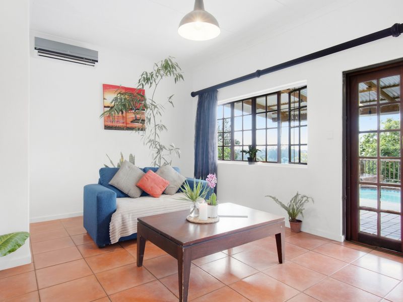 A bright living room featuring terracotta floor tiles, a split-system air conditioner, and direct access to an outdoor patio area through a timber-framed glass door.