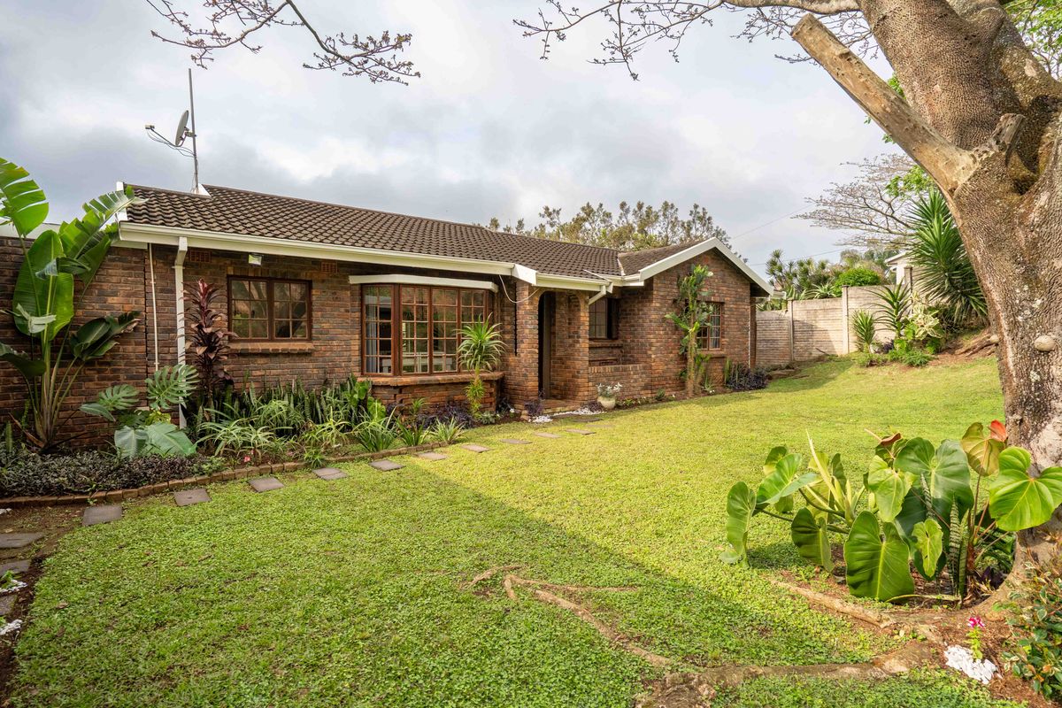 A well-maintained face brick house exterior featuring a tiled roof, bay window, and a spacious, landscaped rear garden with mature trees.