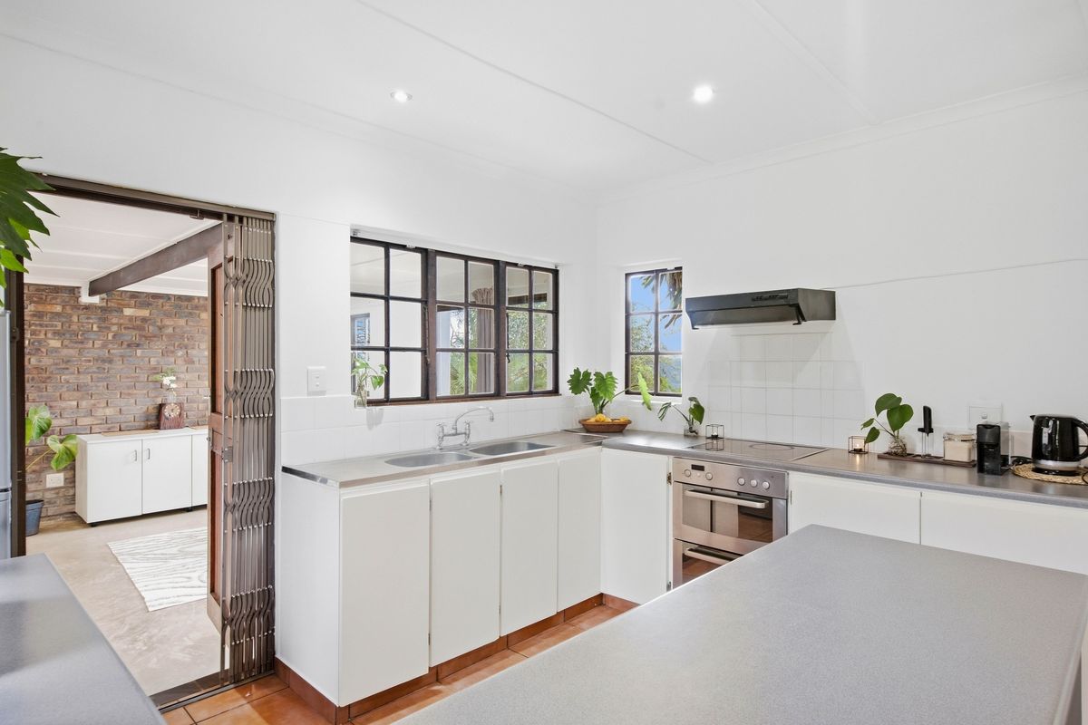 A functional kitchen featuring white cabinetry, stainless steel sink, built-in oven, and cooktop, with a metal security gate leading to an adjacent living area.