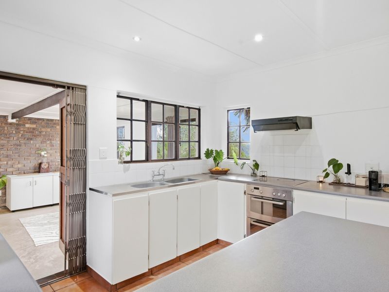 A functional kitchen featuring white cabinetry, stainless steel sink, built-in oven, and cooktop, with a metal security gate leading to an adjacent living area.