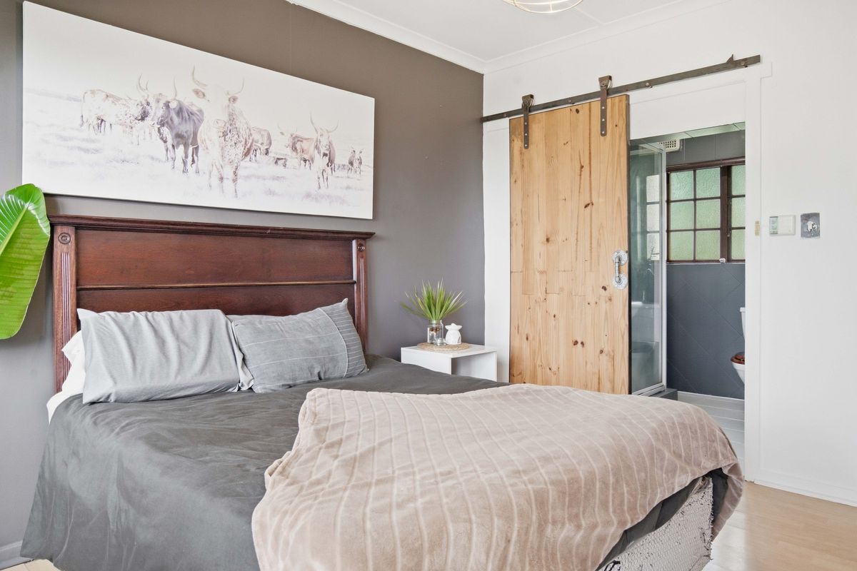 A well-maintained bedroom featuring laminate flooring, a coved ceiling, and a rustic sliding barn door providing access to an en-suite bathroom.