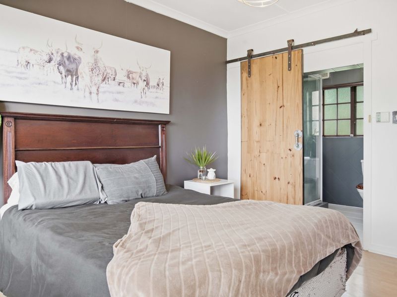 A well-maintained bedroom featuring laminate flooring, a coved ceiling, and a rustic sliding barn door providing access to an en-suite bathroom.