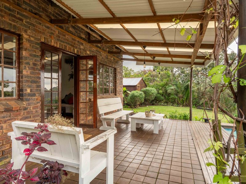 A covered outdoor patio featuring exposed brick walls, tiled flooring, and timber-framed glass doors leading into the home, overlooking a garden area.