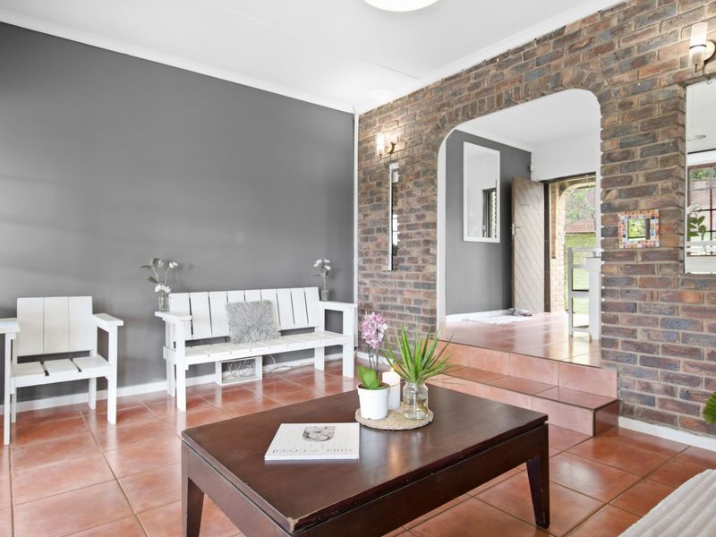 A living room featuring a distinctive exposed brick archway, ceramic tile flooring, and a raised transition area leading to the entrance.