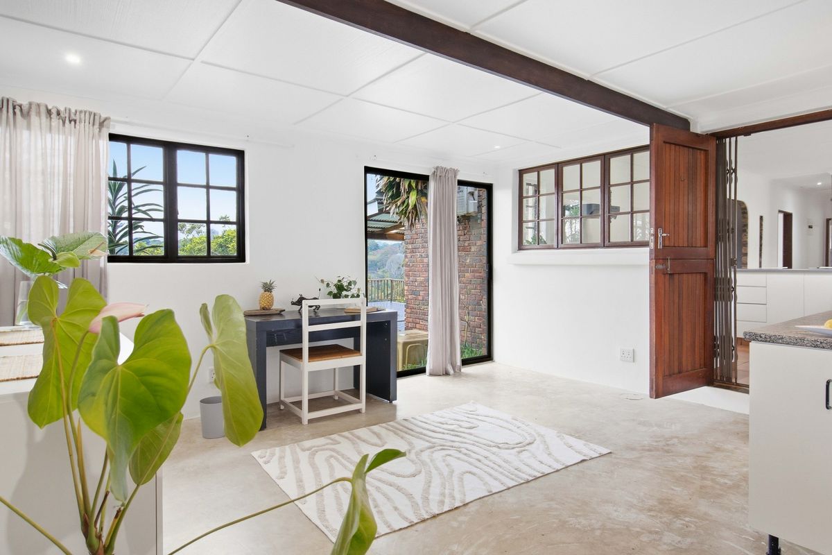 Bright living area featuring exposed ceiling beams, polished tiled flooring, and direct access to the outdoor space through a sliding glass door.