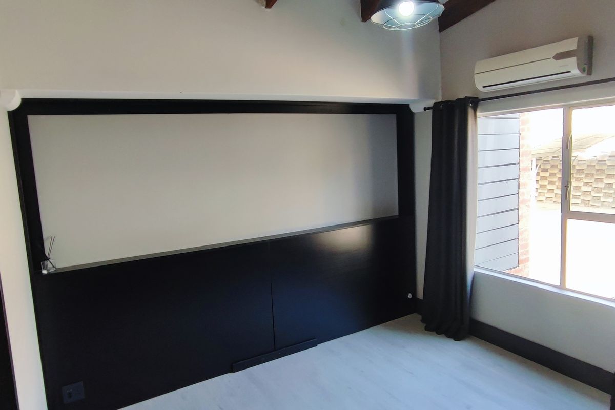 A bright, empty bedroom featuring modern black wall paneling, exposed timber ceiling beams, laminate flooring, and a wall-mounted split-system air conditioner.