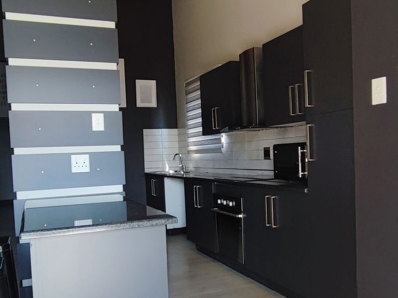 Modern kitchen featuring dark cabinetry, built-in oven and hob, tiled backsplash, and striking exposed timber ceiling beams in an open-plan layout.