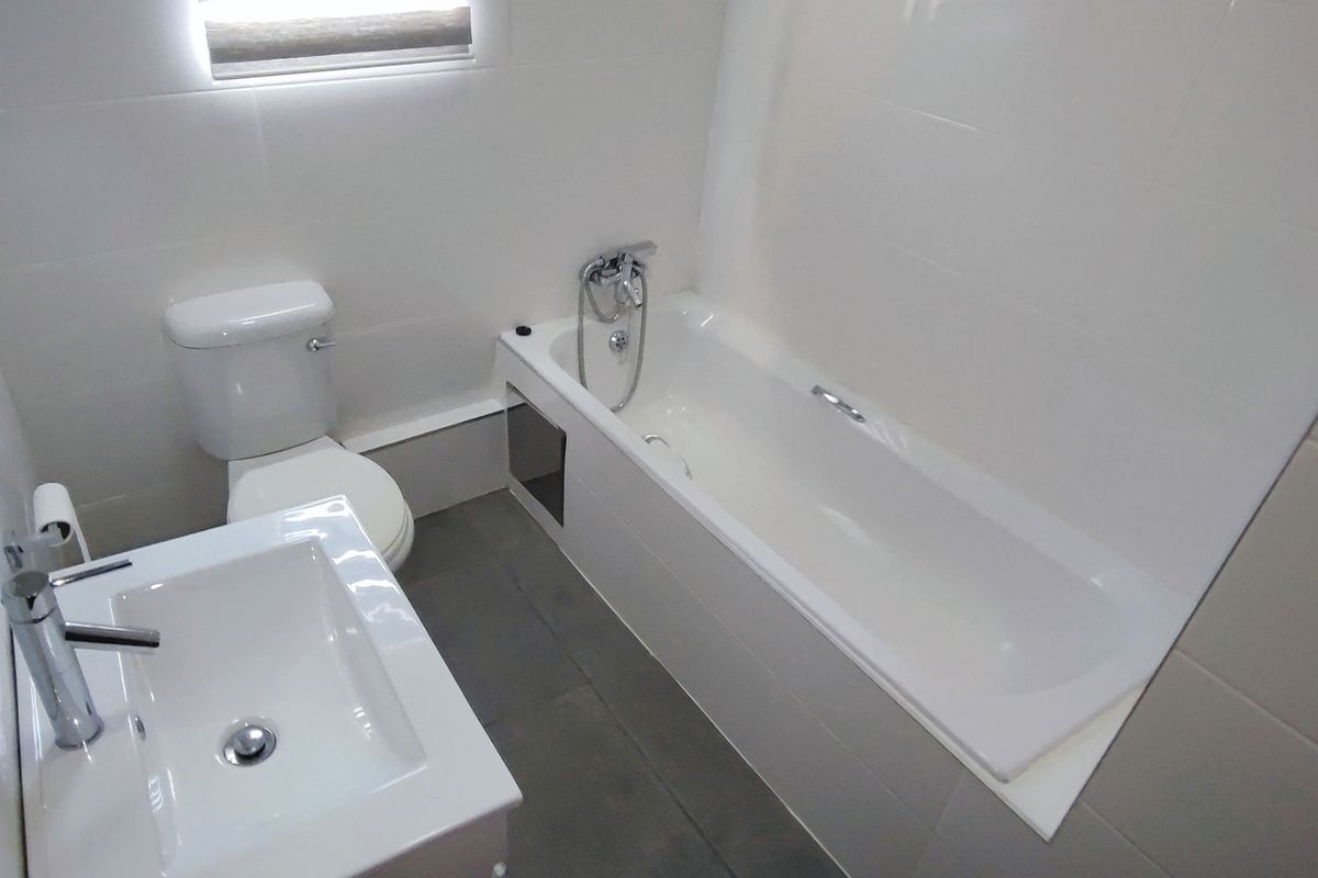 A clean, modern bathroom featuring a white bathtub, a contemporary vanity basin with a mixer tap, and neutral wall and floor tiling.