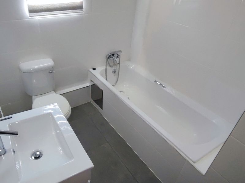 A clean, modern bathroom featuring a white bathtub, a contemporary vanity basin with a mixer tap, and neutral wall and floor tiling.