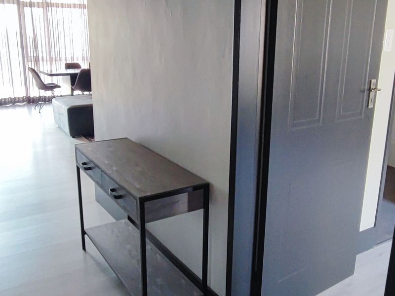A clean hallway featuring light-toned laminate flooring, a wall-mounted electrical distribution board, and a dark-finished internal door leading to an adjacent room.