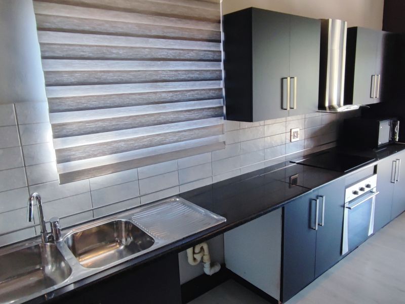 Modern kitchen featuring dark cabinetry, black stone countertops, stainless steel sink, built-in oven, extractor fan, and tiled backsplash.