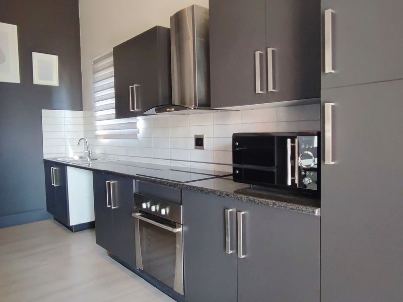 Modern kitchen featuring dark grey cabinetry, granite countertops, stainless steel appliances, and a clean tiled backsplash in a well-maintained apartment setting.