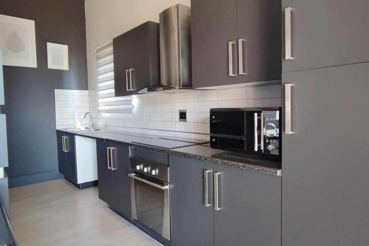 Modern kitchen featuring dark grey cabinetry, granite countertops, stainless steel appliances, and a clean tiled backsplash in a well-maintained apartment setting.