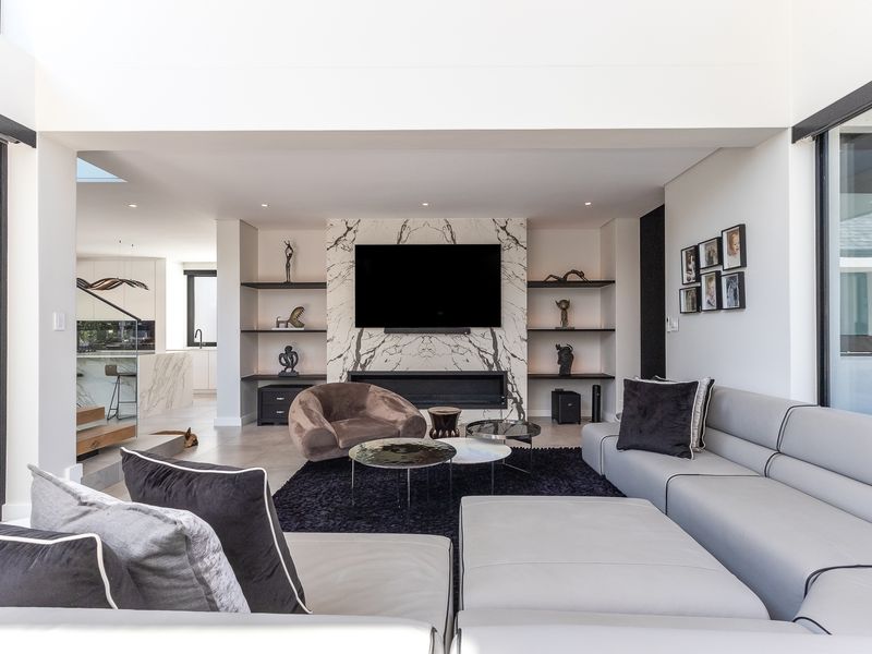 Modern open-plan living area featuring a striking marble fireplace, built-in shelving, and expansive glass doors that provide seamless indoor-outdoor flow.