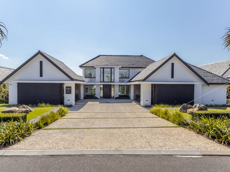 A modern, architecturally designed home featuring a symmetrical facade, double garages, and a spacious paved driveway with manicured landscaping.