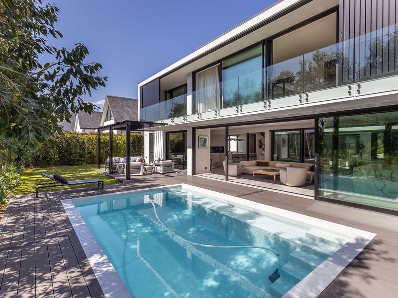 Modern two-story residence featuring a swimming pool, expansive timber decking, and seamless indoor-outdoor flow through large sliding glass doors to the living area.