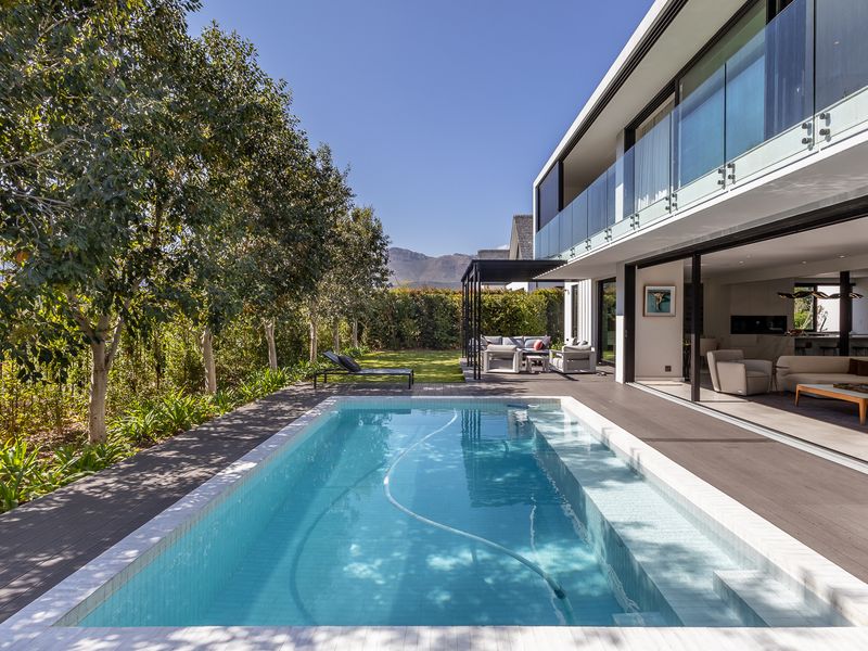 Modern outdoor living area featuring a pristine swimming pool, timber decking, and seamless indoor-outdoor flow through large sliding glass doors.