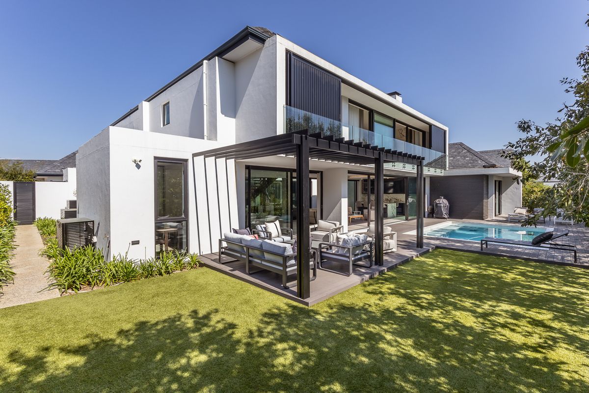 Modern rear exterior featuring a covered pergola, timber decking, swimming pool, and glass balustrades, seamlessly connecting indoor and outdoor living spaces.