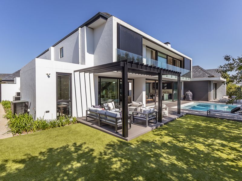 Modern rear exterior featuring a covered pergola, timber decking, swimming pool, and glass balustrades, seamlessly connecting indoor and outdoor living spaces.