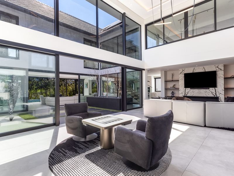 Spacious open-plan living area featuring double-volume ceilings, floor-to-ceiling glass walls, and a striking marble fireplace feature, seamlessly connecting to the outdoor courtyard.