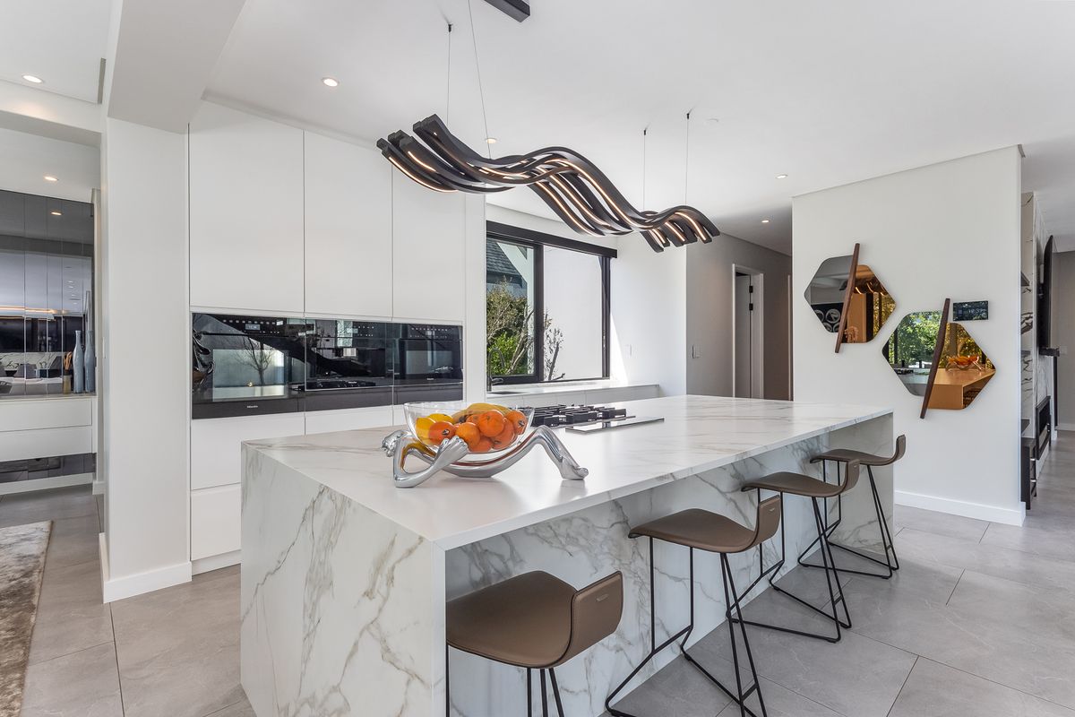 Modern luxury kitchen featuring a large marble waterfall island, integrated high-end appliances, handleless cabinetry, and sophisticated designer lighting.