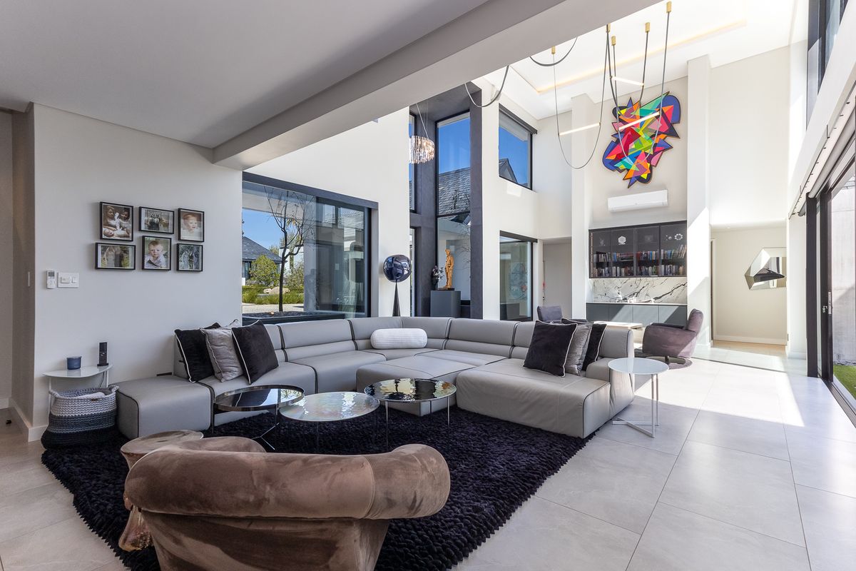 Spacious double-volume living room featuring large format floor tiles, modern built-in cabinetry with marble detailing, and expansive glass doors leading to the outdoors.