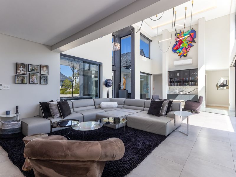 Spacious double-volume living room featuring large format floor tiles, modern built-in cabinetry with marble detailing, and expansive glass doors leading to the outdoors.