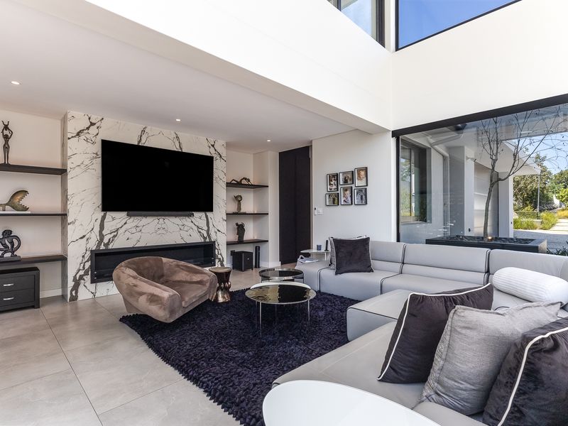 Modern living room featuring a striking marble feature wall with a built-in fireplace, double volume ceilings, and large windows providing natural light.