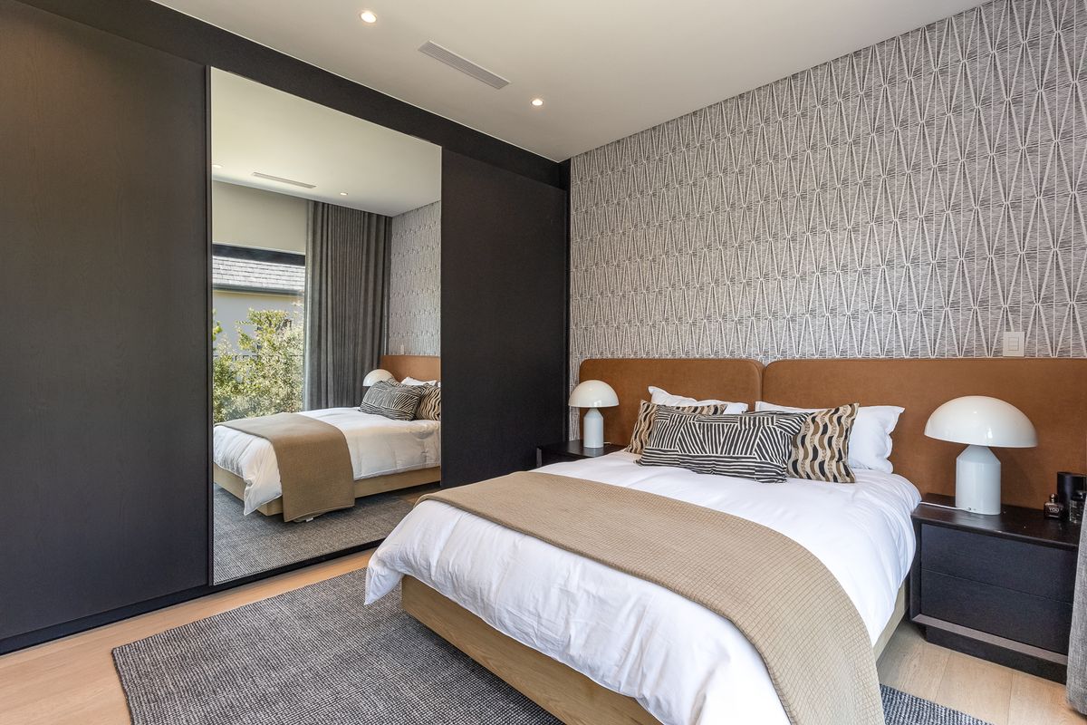 Modern bedroom featuring built-in wardrobes with mirrored doors, patterned accent wallpaper, and recessed ceiling lighting.