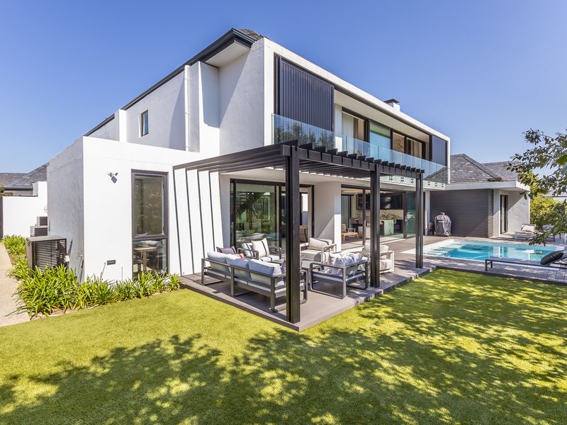 Modern rear exterior featuring a covered pergola, wooden decking, swimming pool, and well-maintained landscaped garden with contemporary architectural finishes.