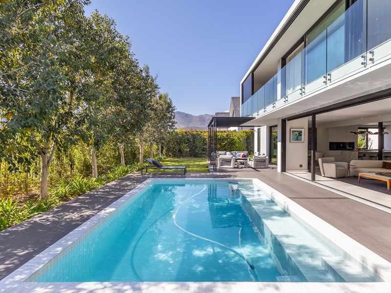 Modern outdoor living area featuring a pristine swimming pool, timber decking, and seamless indoor-outdoor flow through large sliding glass doors.