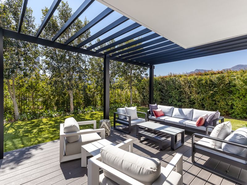 A well-maintained outdoor patio featuring a modern black metal pergola and composite decking, overlooking a private, landscaped garden area.