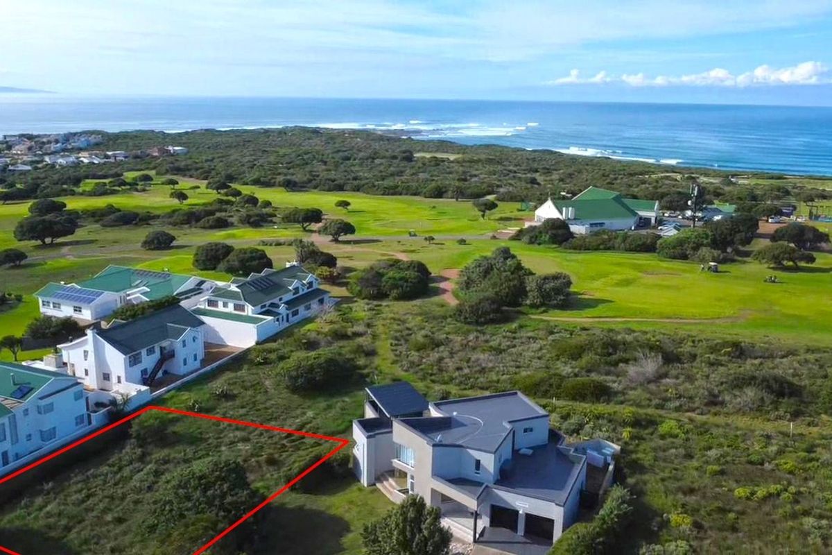 An aerial view of a vacant residential plot situated in a coastal estate, featuring surrounding greenery and proximity to the ocean.