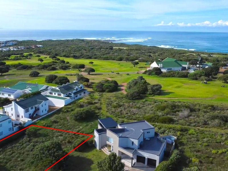 An aerial view of a vacant residential plot situated in a coastal estate, featuring surrounding greenery and proximity to the ocean.