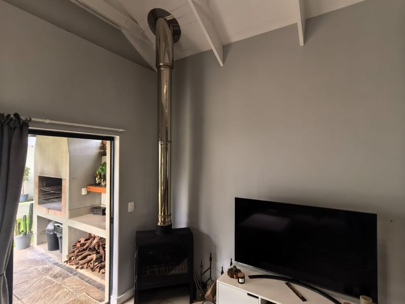 Living room featuring a freestanding fireplace, exposed rafters, and tiled flooring, with direct access to an outdoor patio area.