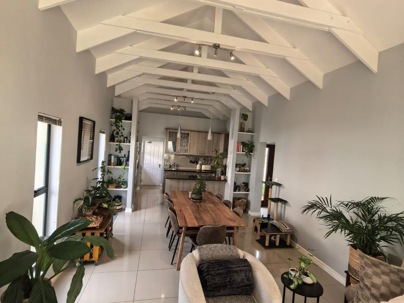 Spacious open-plan living and dining area featuring a striking vaulted ceiling with exposed white timber trusses and modern tiled flooring.