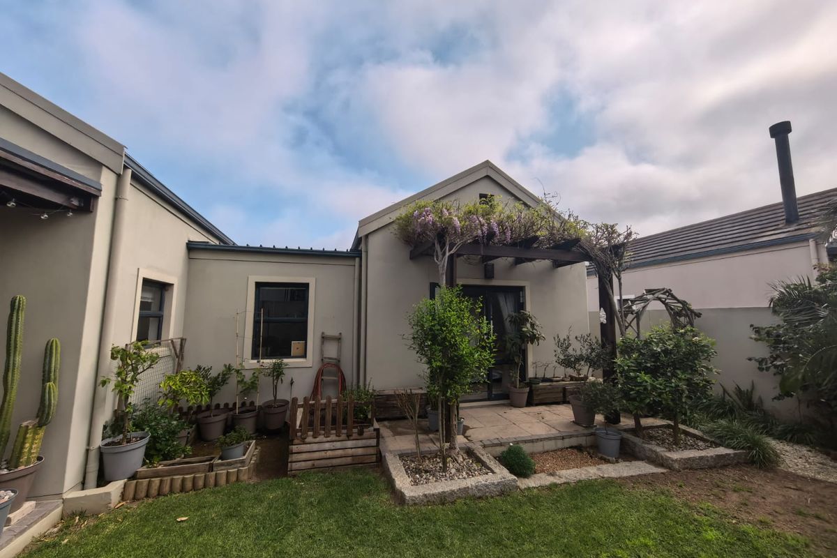 Rear exterior view featuring a paved patio area with a timber pergola, stone garden borders, and a well-maintained lawn.