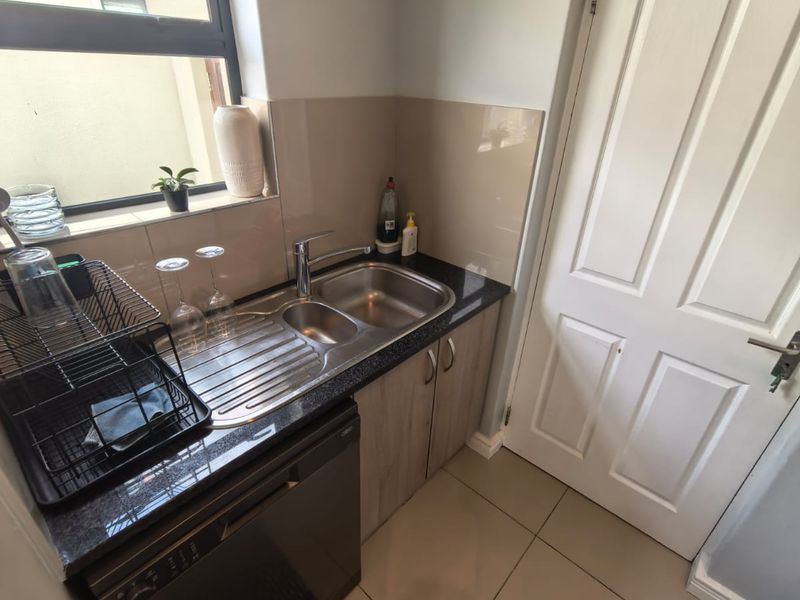 A functional scullery area featuring a stainless steel double sink, integrated dishwasher, granite countertops, and tiled splashback.