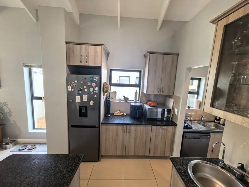 A functional kitchen featuring wood-look cabinetry, granite countertops, tiled flooring, and a vaulted ceiling, providing a practical workspace with integrated sink and storage.